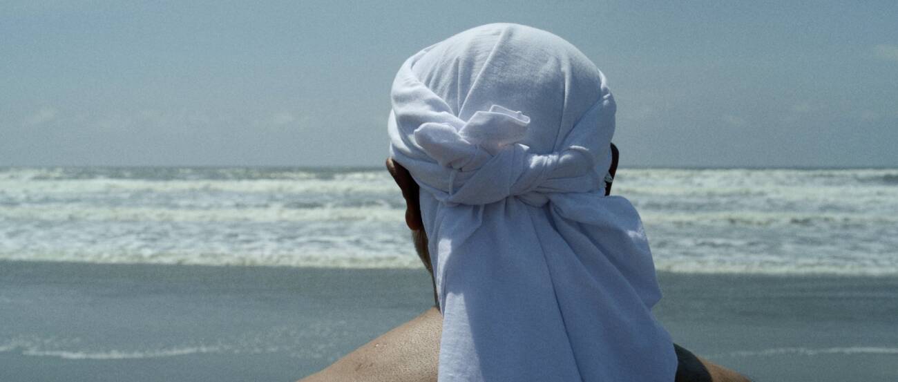 Pessoa na praia com pano branco na cabeça.