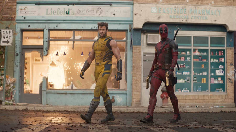Dois super-heróis caminham em frente à loja e farmácia.