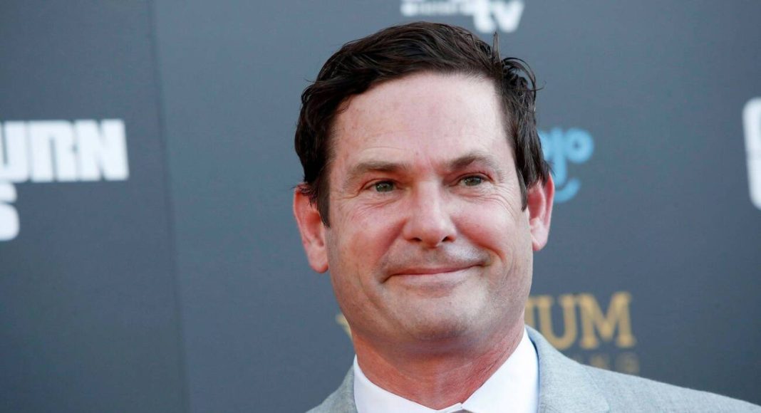 henry thomas Homem sorrindo de terno cinza em evento.