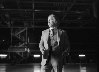 Homem elegante em cenário industrial preto e branco.