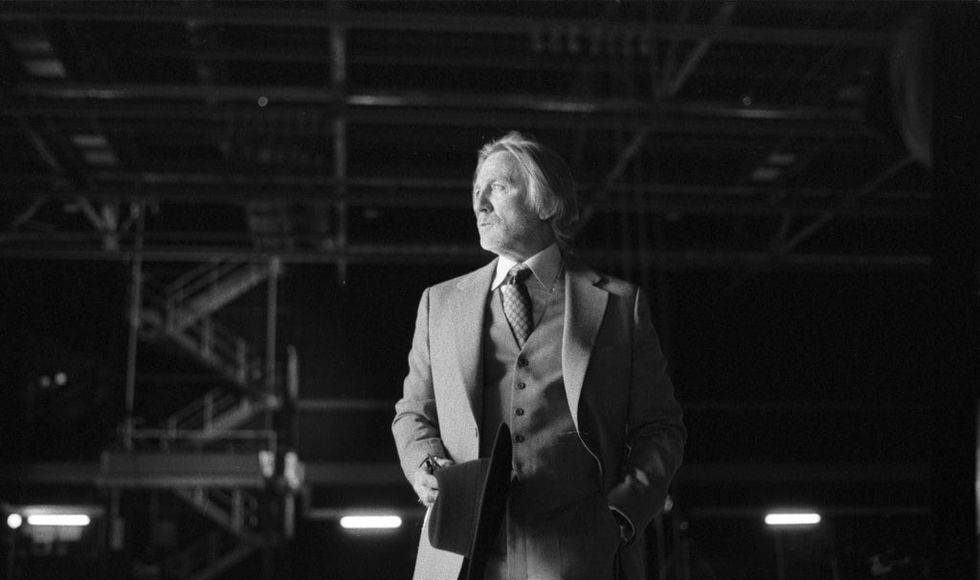 Homem elegante em cenário industrial preto e branco.