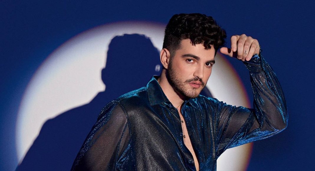 Homem posando com camisa brilhante diante de luz circular.