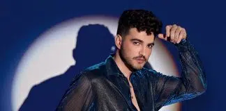 Homem posando com camisa brilhante diante de luz circular.