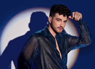 Homem posando com camisa brilhante diante de luz circular.