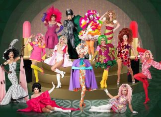 Drag queens em fantasias coloridas posam em palco decorado.