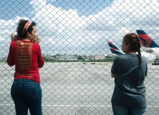 Duas pessoas observando aviões através de uma cerca.