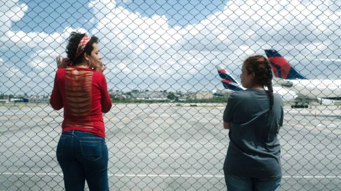 Duas pessoas observando aviões através de uma cerca.