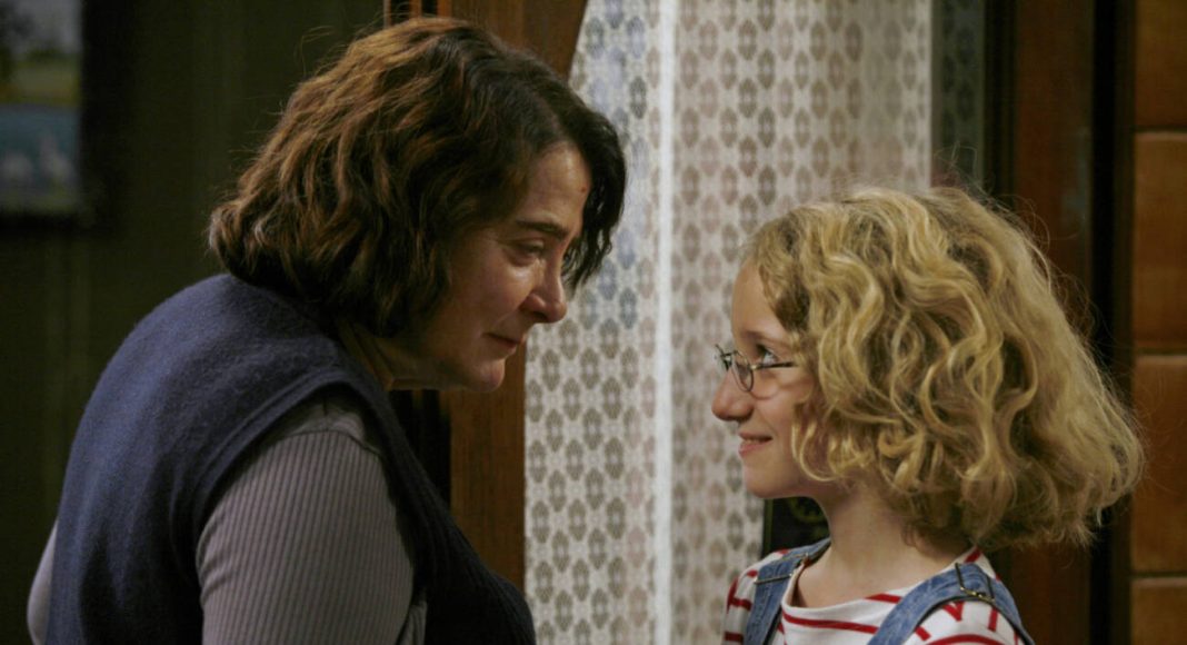 Mulher conversando com criança loira usando óculos.