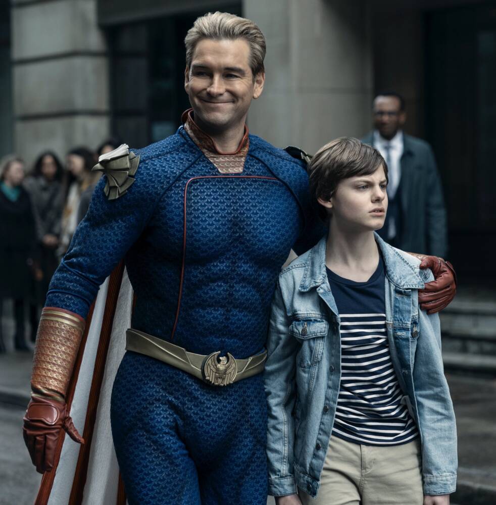 Super-herói sorrindo ao lado de jovem em uma rua.