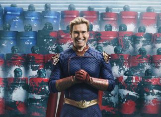 Homem de uniforme de super-herói sorrindo em frente a escudos coloridos.