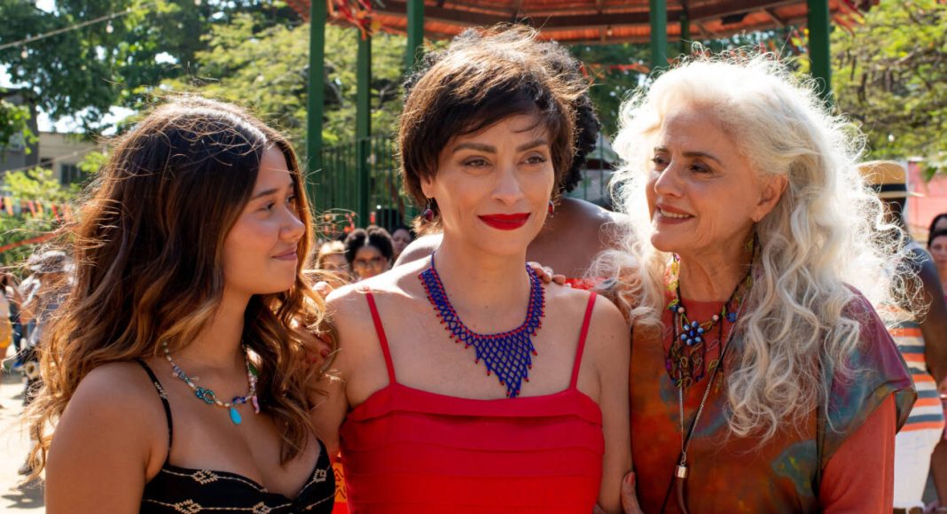 Três mulheres sorrindo em festa ao ar livre.