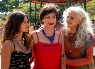 Três mulheres sorrindo em festa ao ar livre.
