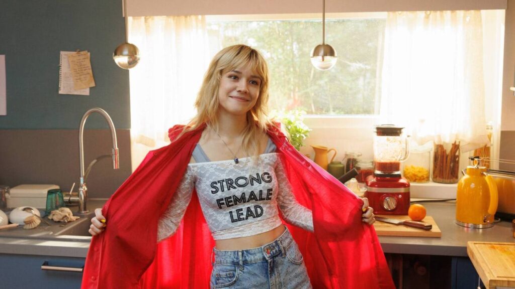 Mulher com camiseta 'Strong Female Lead' na cozinha.