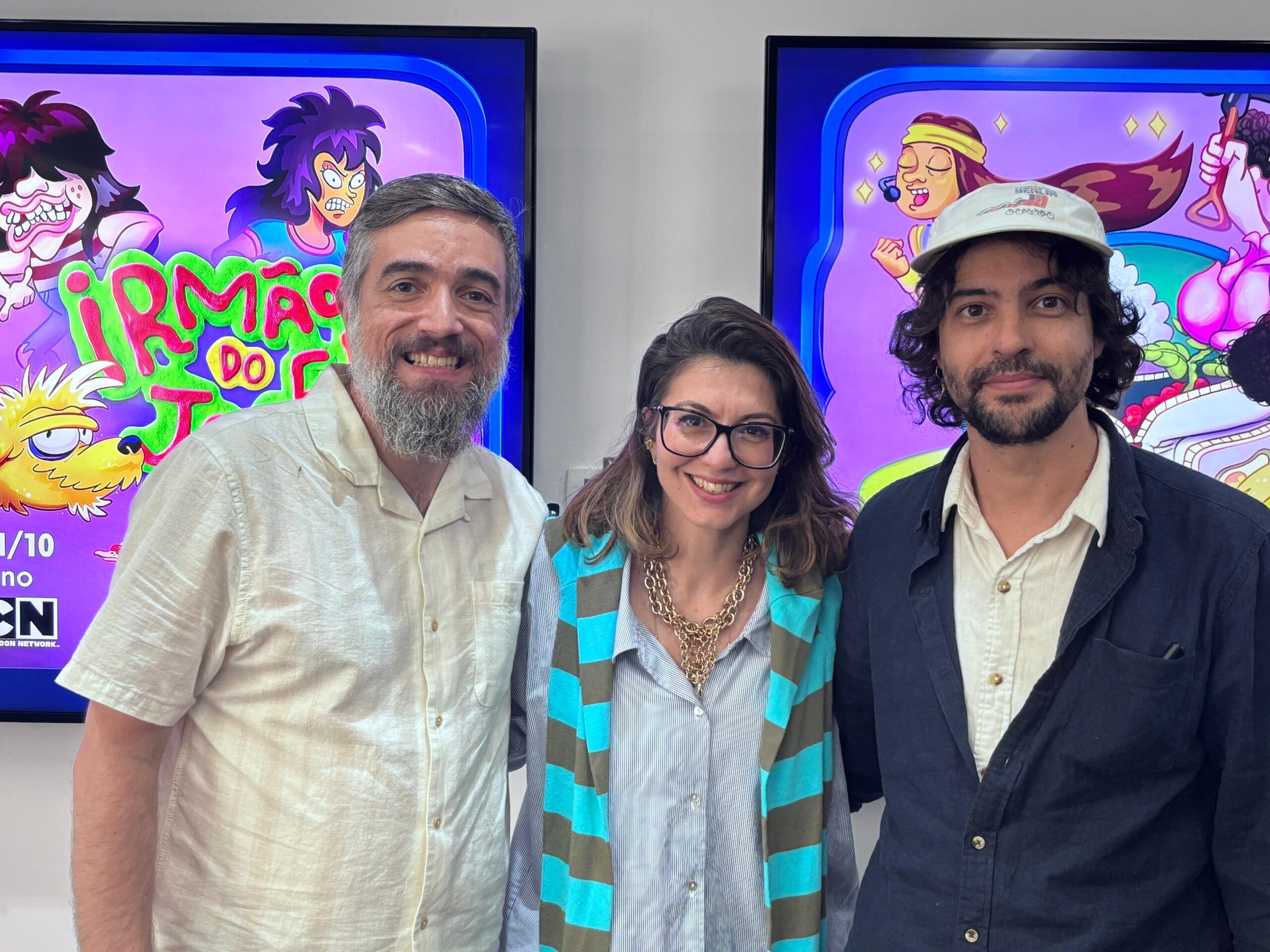 Três pessoas sorrindo na frente de cartaz colorido.