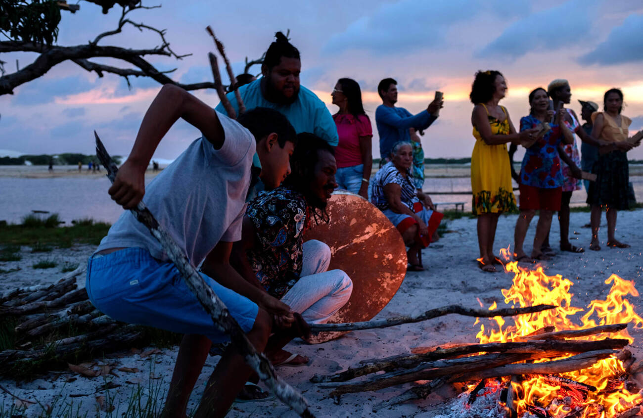 Pessoas celebram ao redor de uma fogueira na praia.