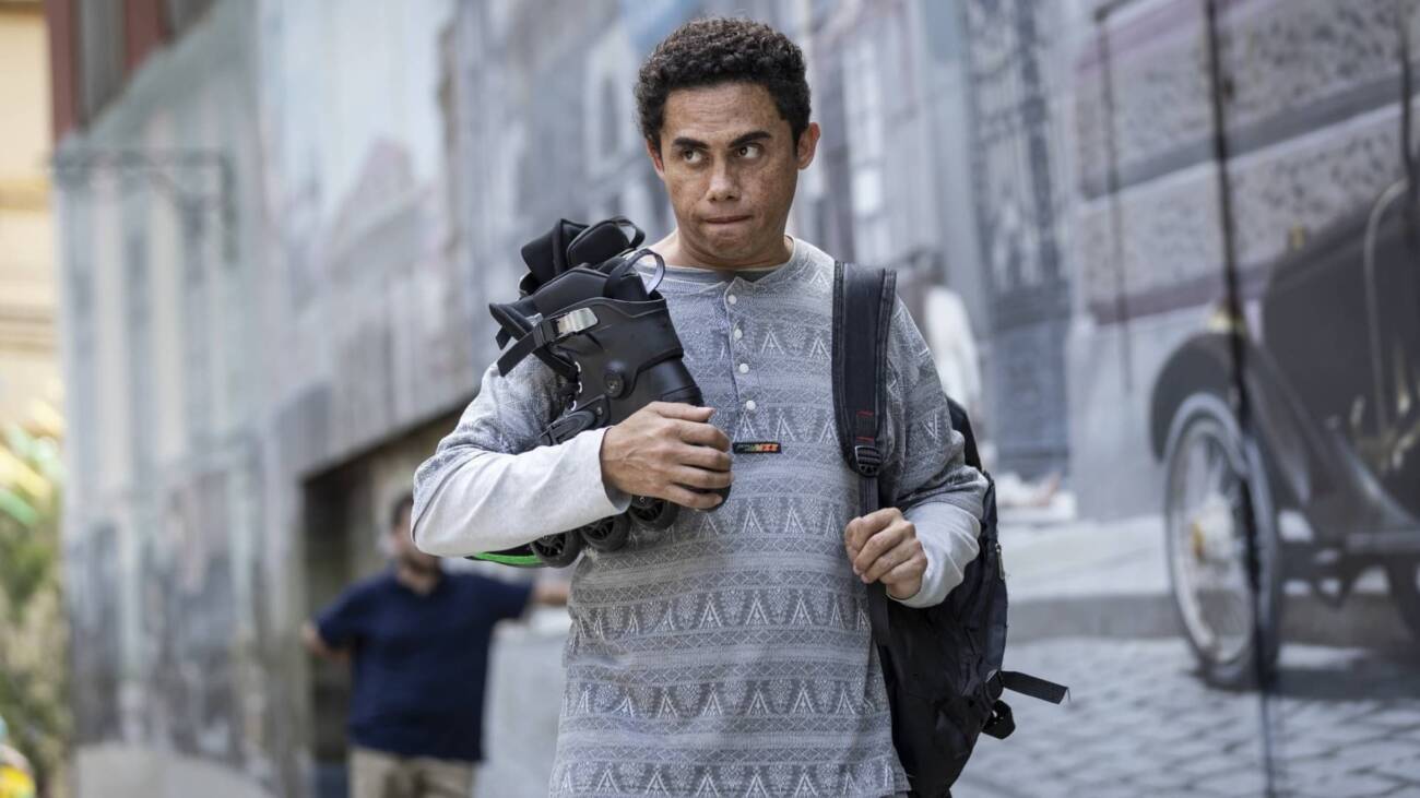 Homem carregando patins na rua, fundo urbano.