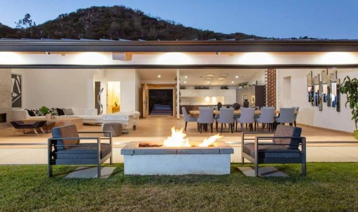 Casa moderna com &aacute;rea externa iluminada e fogueira.