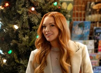 Lindsay Lohan estampa cartaz inédito da comédia natalina ‘Nosso Segredinho’ Mulher sorrindo ao lado de árvore de Natal.