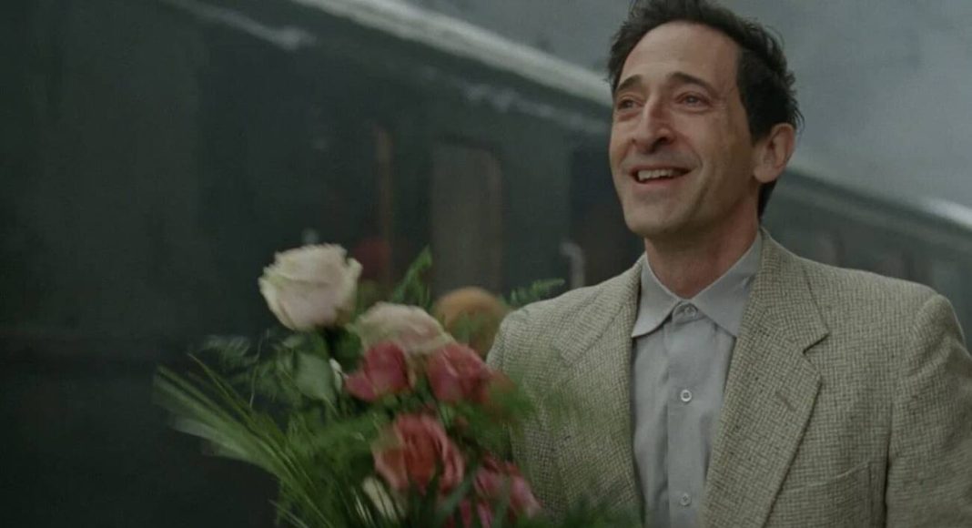 Homem sorrindo segurando buquê de flores na estação.