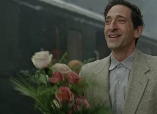 Homem sorrindo segurando buquê de flores na estação.