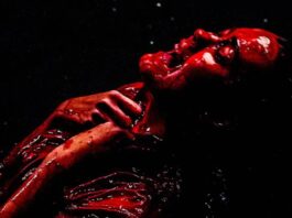 Pessoa coberta de tinta vermelha, expressão intensa.