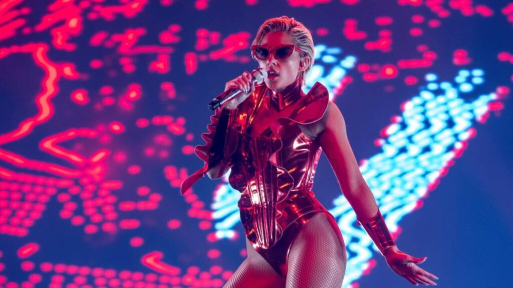 Cantora performa em palco iluminado, vestida de vermelho.