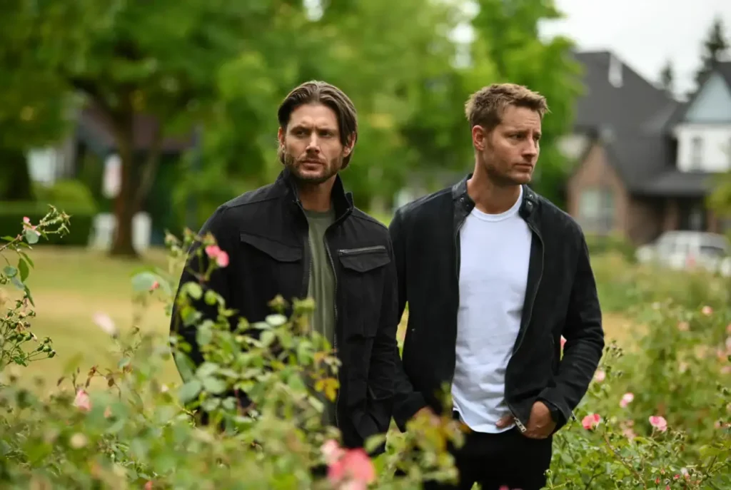 Dois homens em jardim com flores rosas.