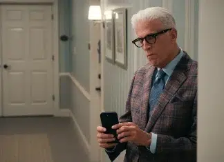 Homem de óculos com celular em ambiente interno.