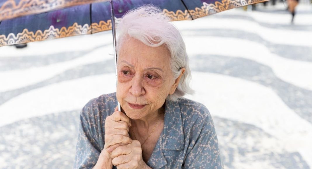 Idosa com guarda-chuva na calçada de mosaico.