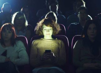 Mulher usando celular iluminada no cinema escuro