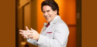 Homem sorridente em terno branco estendendo as mãos