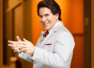 Homem sorridente em terno branco estendendo as mãos