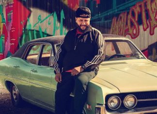 Homem sentado em carro vintage, fundo com grafite colorido