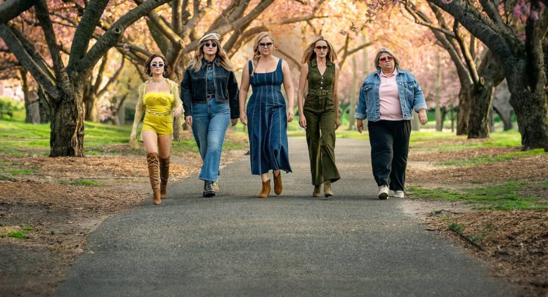 Mulheres estilosas caminhando em parque florido.