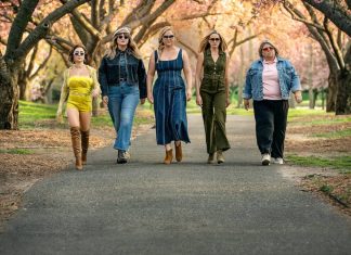 Mulheres estilosas caminhando em parque florido.