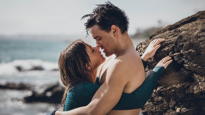 Casal se beijando na praia ao lado de uma rocha