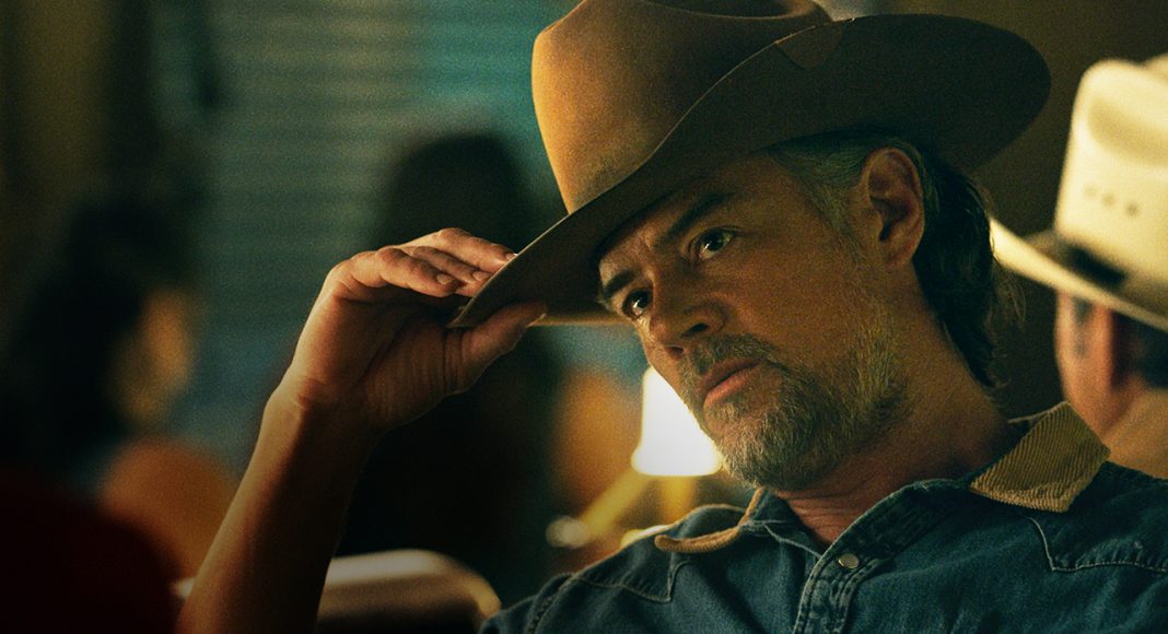 Homem segurando chapéu de cowboy em ambiente iluminado