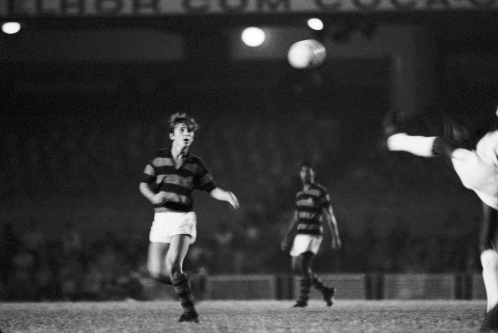 Soccer players in striped jerseys on a night field; ball is in midair as a keeper dives to save.