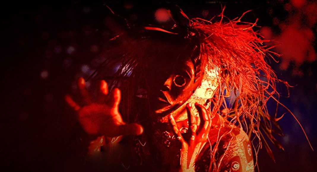 A masked, horror-style figure with straw-like hair reaching toward the camera in red lighting.