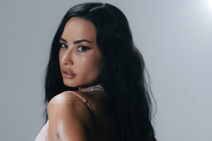 Woman with long black hair looks over her shoulder, wearing a pink top and a beaded necklace against a gray background.