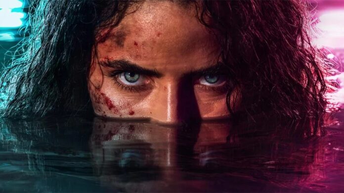 Close-up of a person with blue eyes staring over waterline, blood on the cheek, dark wet hair, under neon blue and pink lighting.