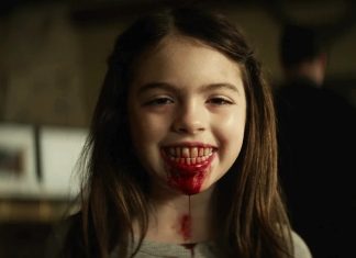 ‘Maldição da Múmia’ se passa no mesmo universo de ‘A Morte do Demônio: A Ascensão’, revela diretor Young girl smiling with blood on her lips and chin in a dimly lit room, suggesting a horror or Halloween scene.