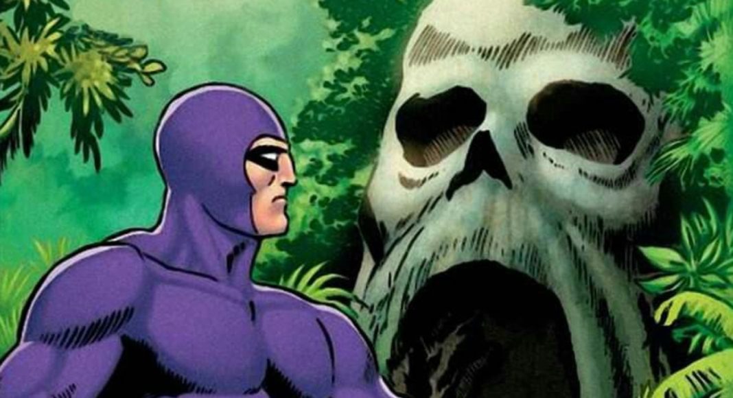 Purple-costumed superhero stands in a jungle, facing a massive skull-shaped rock opening.