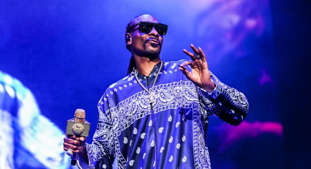 snoop dogg Male performer on stage wearing a blue paisley-pattern shirt and sunglasses, holding a glittering microphone.