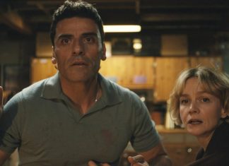 Two adults in a dimly lit kitchen/basement look terrified and alert, as if facing danger together.