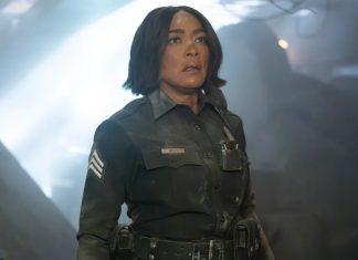 Female officer in a dark uniform with sergeant stripes stands in a smoky, dramatic scene, looking upward with a concerned expression.