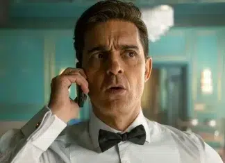 Man in a white dress shirt and black bow tie on a cell phone, looking surprised in a teal-lit room.