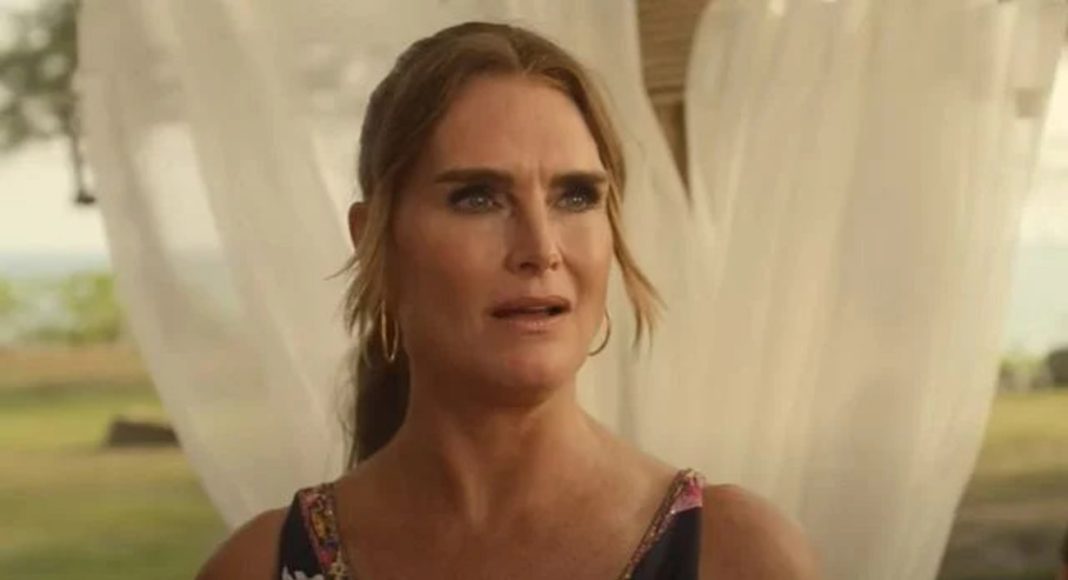 Concerned woman with hoop earrings in a floral dress outdoors, framed by sheer white curtains behind her.