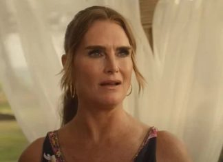 Concerned woman with hoop earrings in a floral dress outdoors, framed by sheer white curtains behind her.