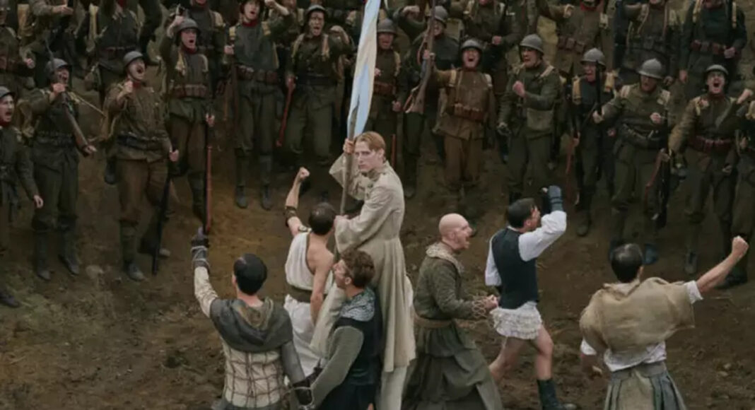 A pale-robed man at the center holds a blue flag as soldiers close in with weapons around him in a chaotic battle on a muddy ground.